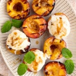 grilled peaches with scoops of ice cream on top and mint leaves for garnish on a white oval serving plate.