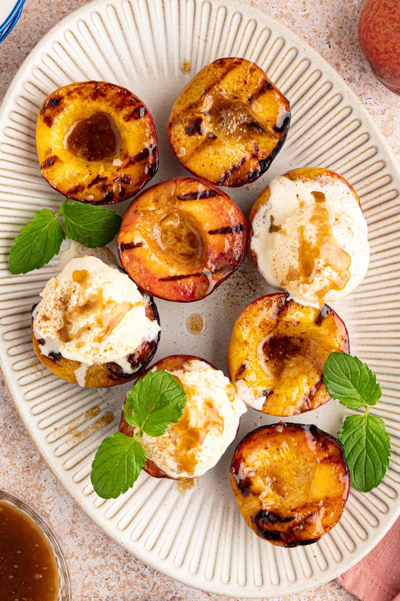 grilled peaches with scoops of ice cream on top and mint leaves for garnish on a white oval serving plate.