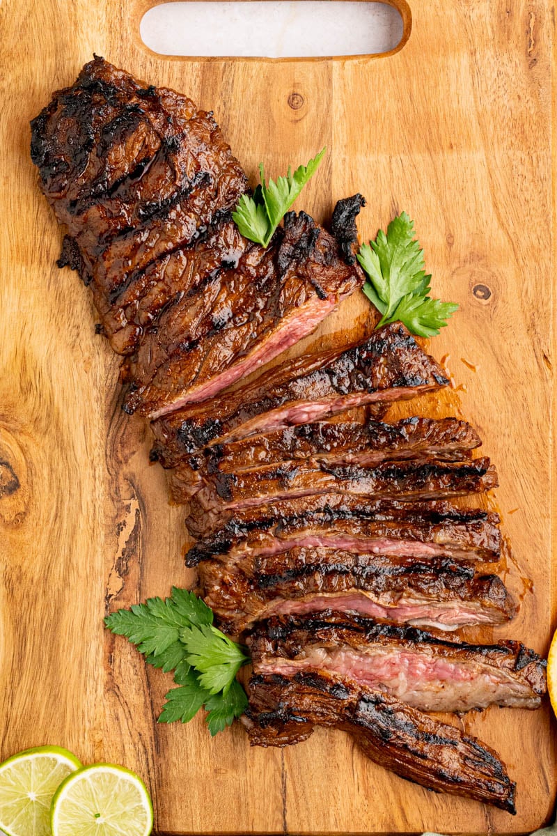 Grilled skirt steak sliced on a wooden cutting board for serving. 