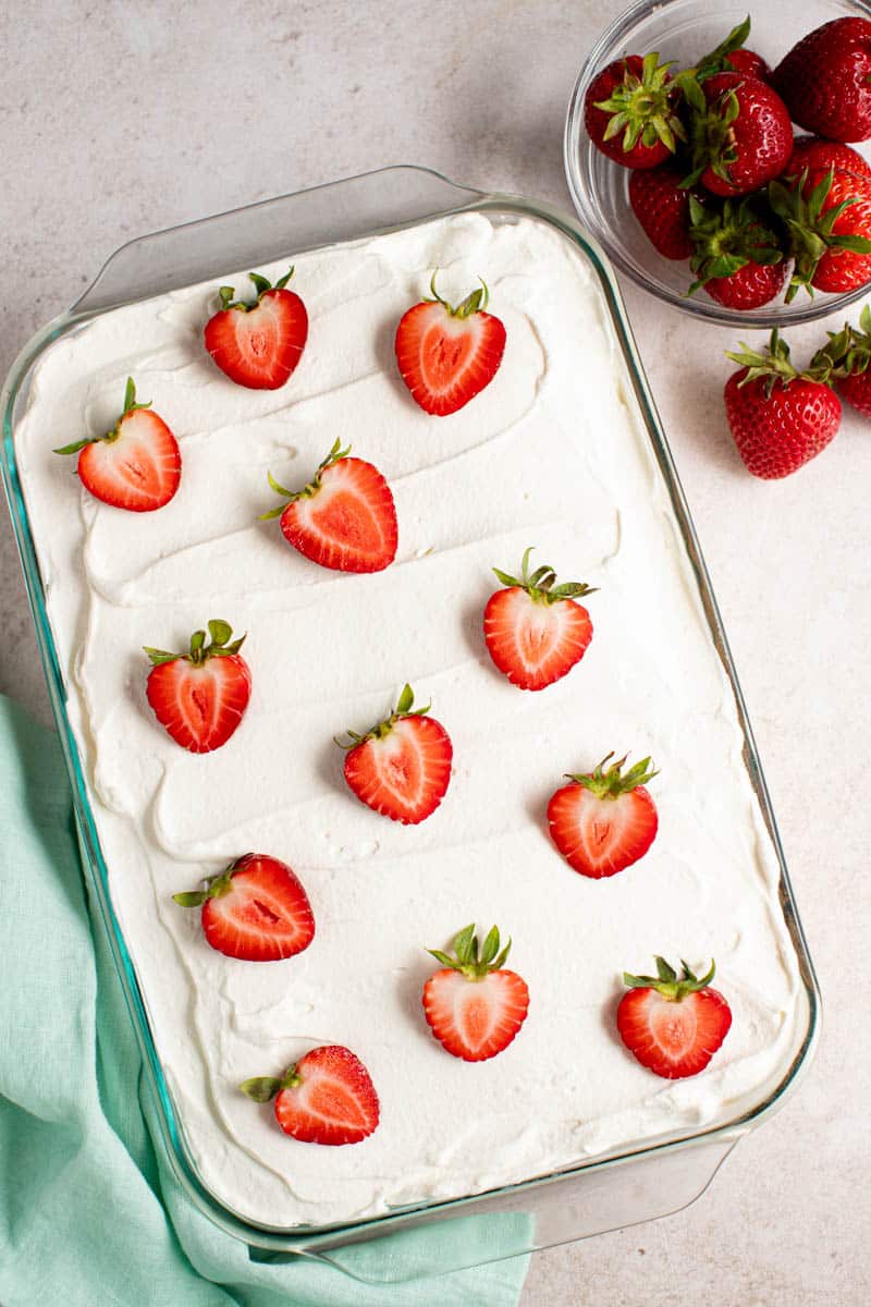 a whole strawberry tres leches cake on a counter for serving. 