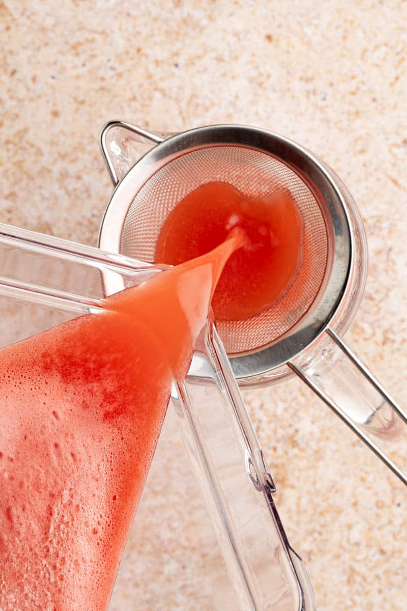 straining the pureed watermelon mixture through a strainer into a pitcher