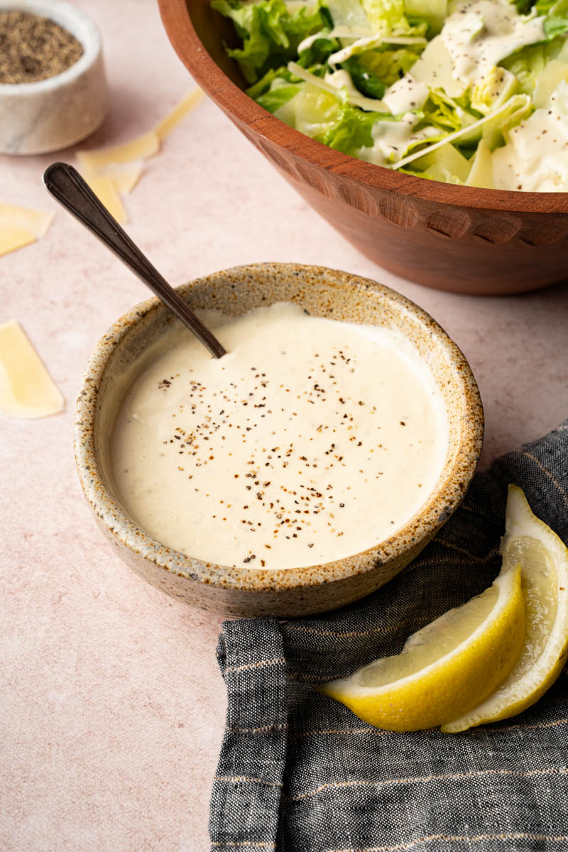 Homemade caesar salad in a small bowl on a countertop next to a bowl of romaine and parmesan cheese.