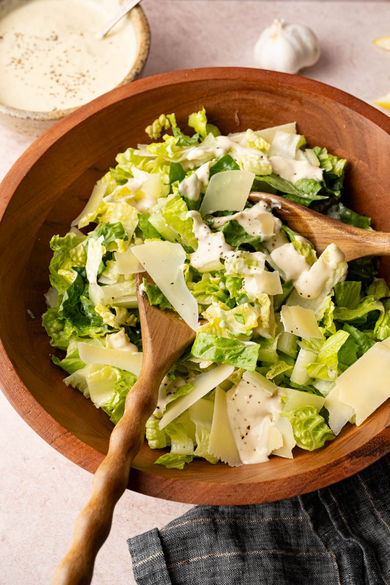 Tossing together the romaine lettuce, parmesan cheese and homemade caesar dressing in a wooden bowl before serving.