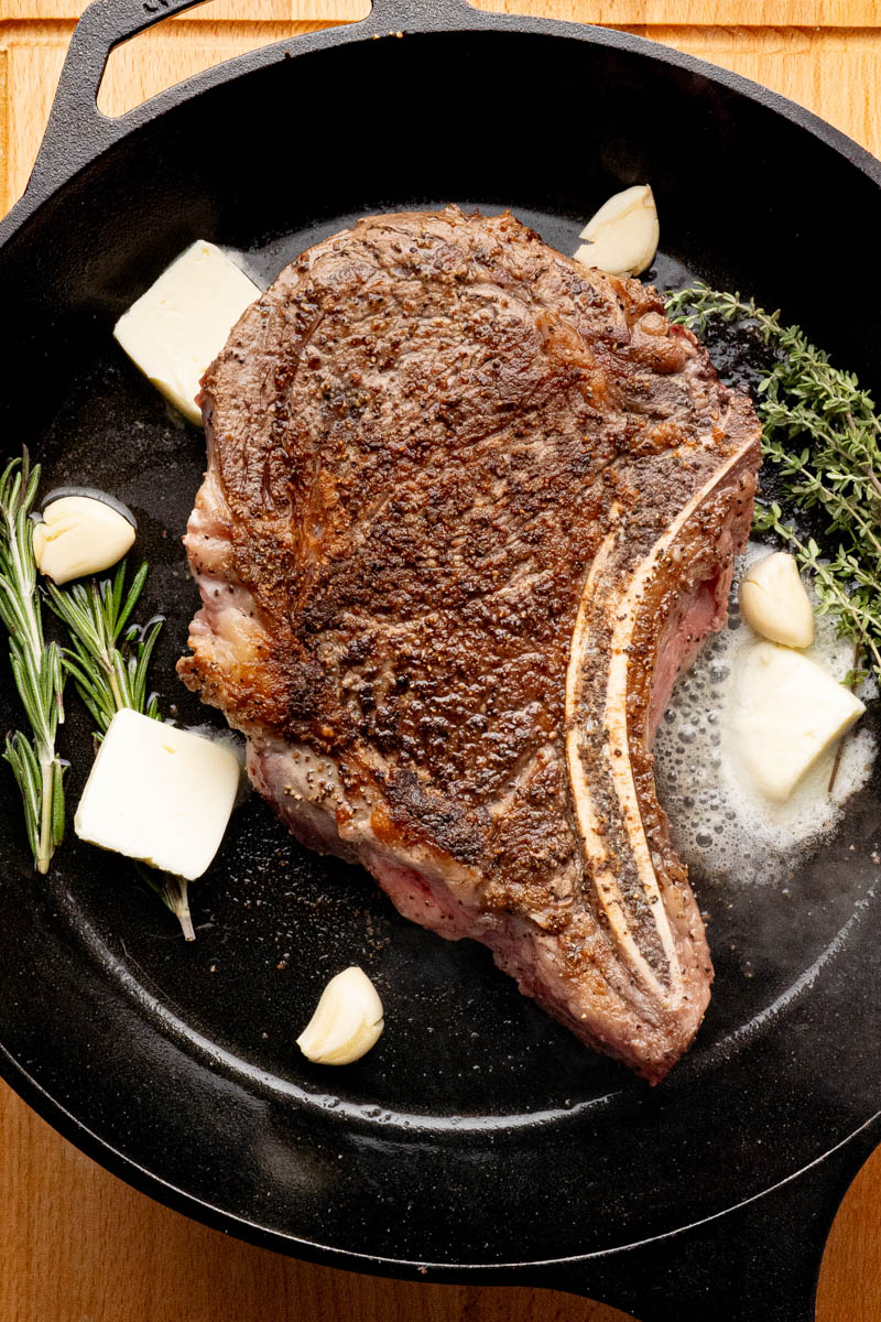 The butter, garlic, rosemary and thyme in the pan with the seared ribeye steak.
