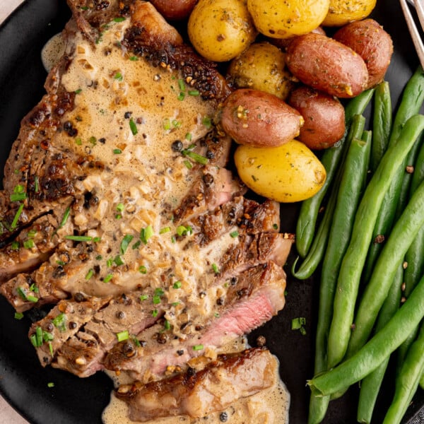 Steak au poivre on a black plate with potatoes and green beans.