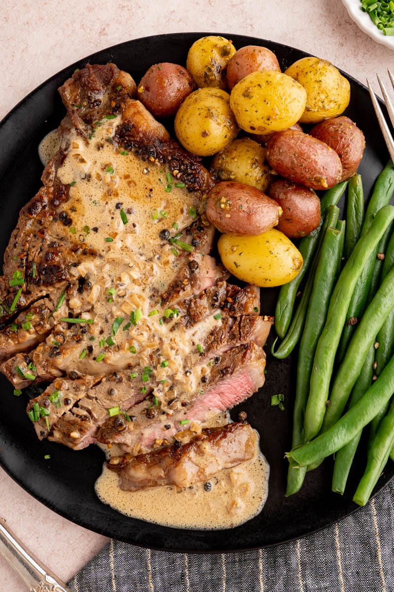 Steak au poivre on a black plate with potatoes and green beans.