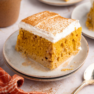 A piece of pumpkin tres leches sits on a white plate with a spoon off to the side for serving.