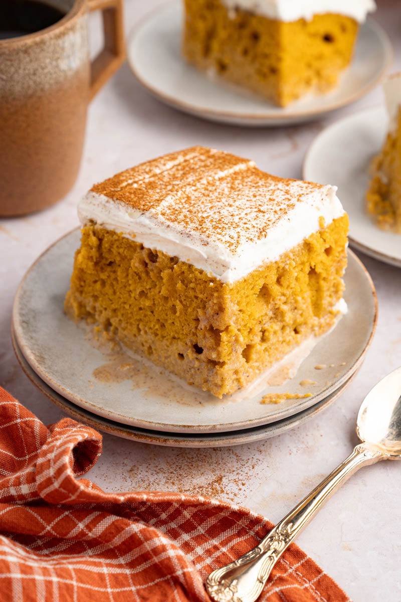 A piece of pumpkin tres leches sits on a white plate with a spoon off to the side for serving.