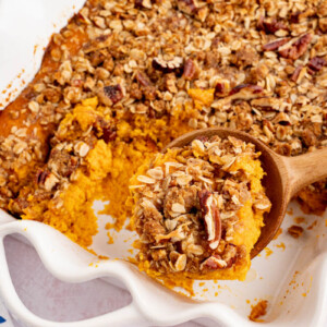 A spoon scoops out a serving of sweet potato casserole from a white rectangular baking dish.
