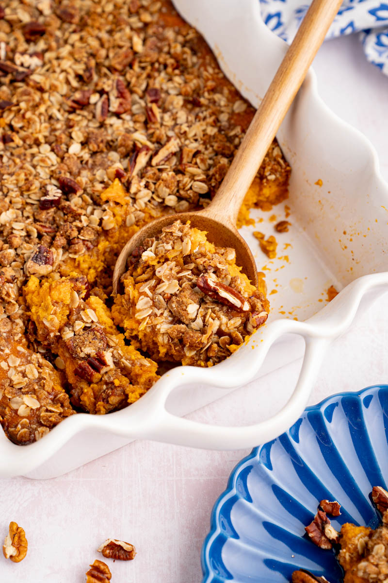 A spoon sits in the baking dish with sweet potato casserole in it, after coming out of the oven. 