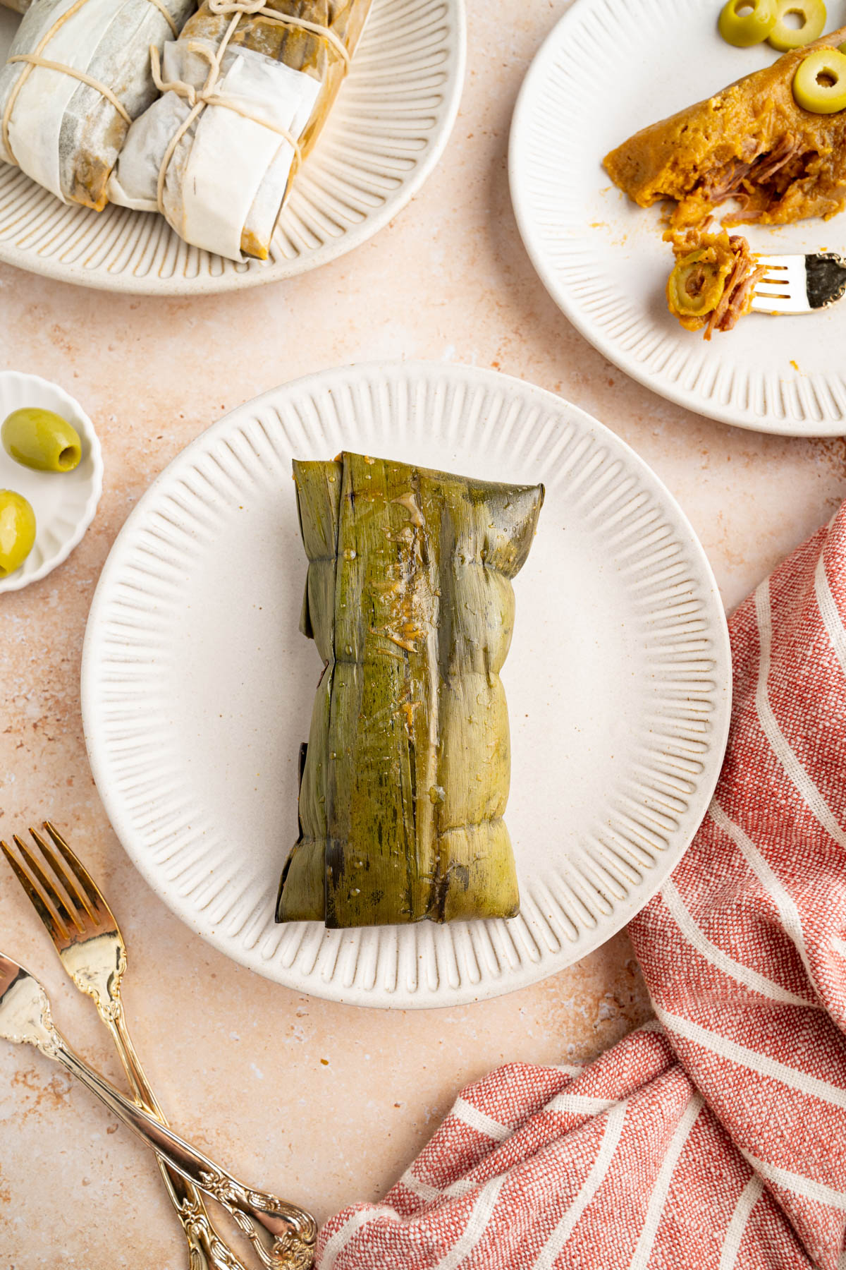 A cooked pastel wrapped in a banana leaf on a white plate.
