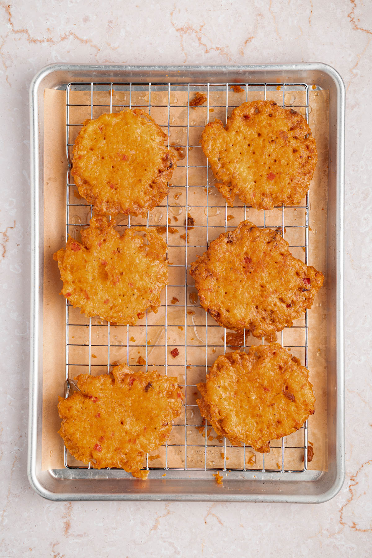 Six bacalaitos or codfish fritters on a baking rack after frying to drain the oil.