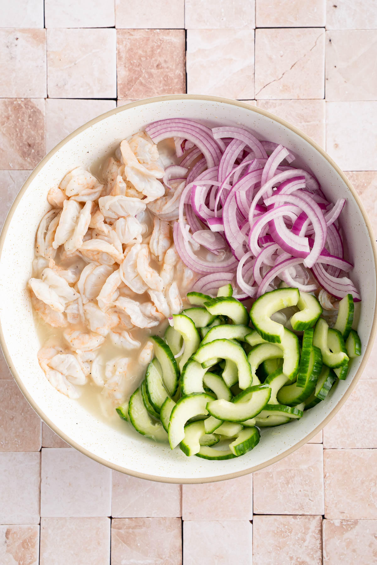 The cooked shrimp, red onion and cucumber in a large bowl before mixing.