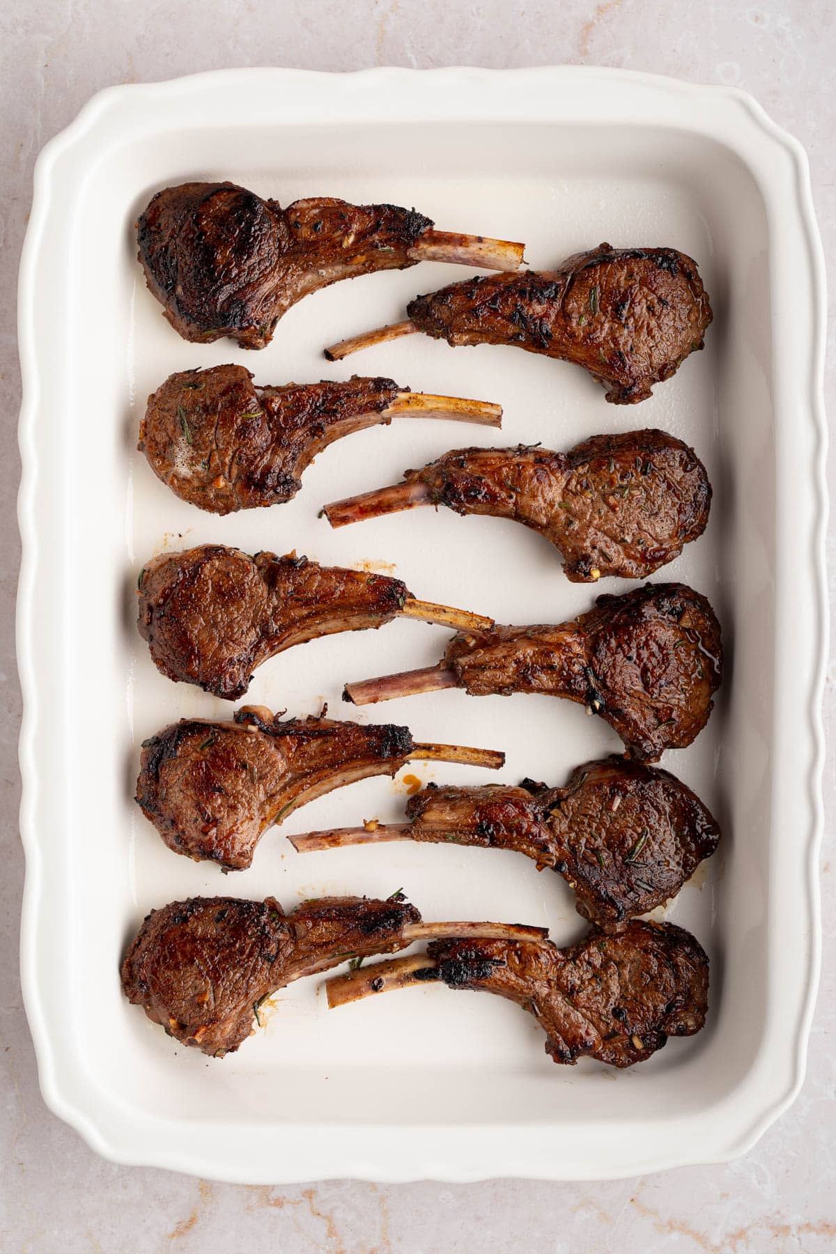 The seared lamb chops in a white baking dish before baking.
