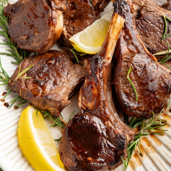 Oven baked lamb chops with balsamic glaze on a serving platter garnished with fresh rosemary and lemon wedges.