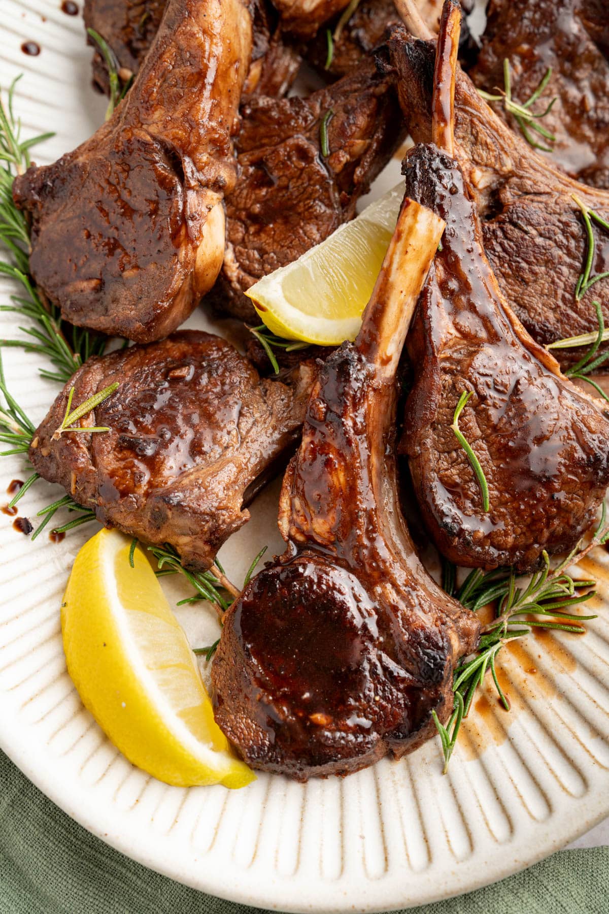 Oven baked lamb chops with balsamic glaze on a serving platter garnished with fresh rosemary and lemon wedges.