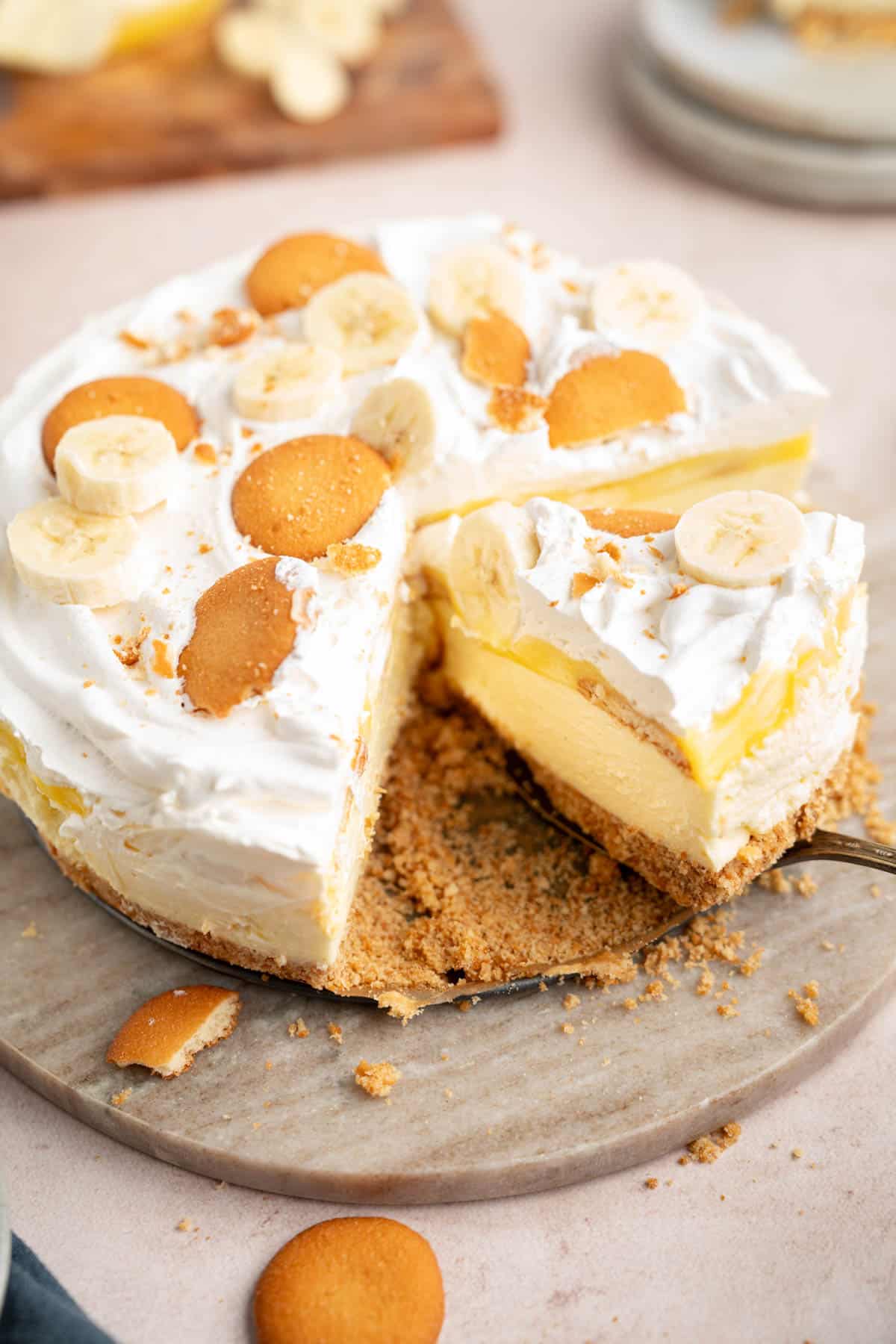A serving knife lifts a slice of the no bake banana pudding cheesecake from the serving plate for serving.