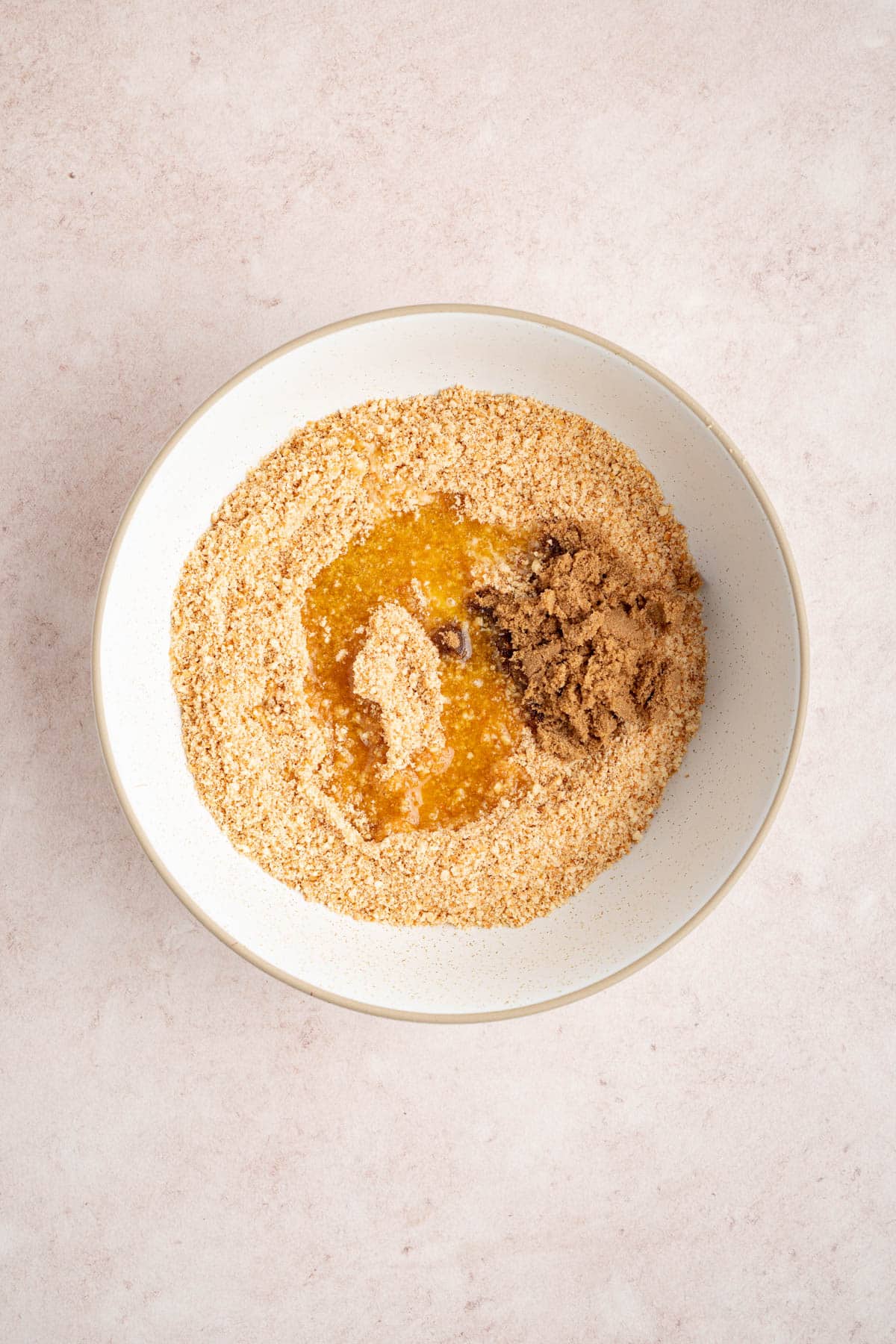The crushed vanilla wafers, brown sugar, and melted butter in white bowl on a countertop before mixing.