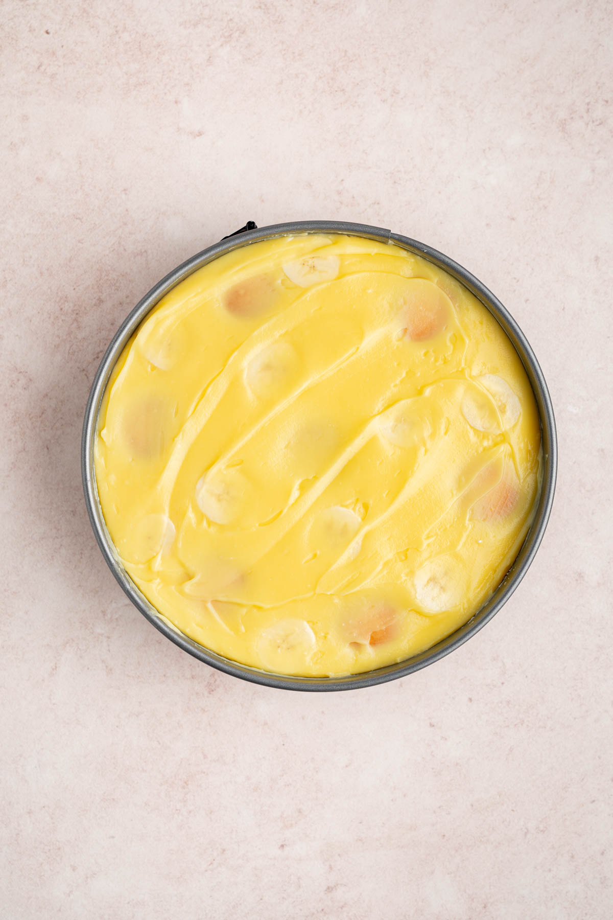 The pudding mix spread over the wafers, banana slices and cheesecake filling in the pan.