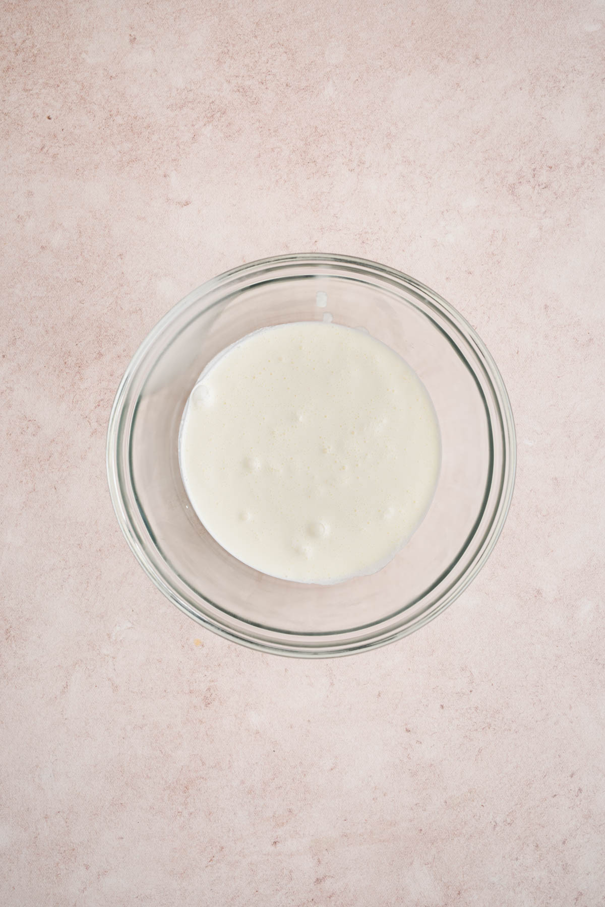 The cold heavy cream in a glass bowl on a countertop.