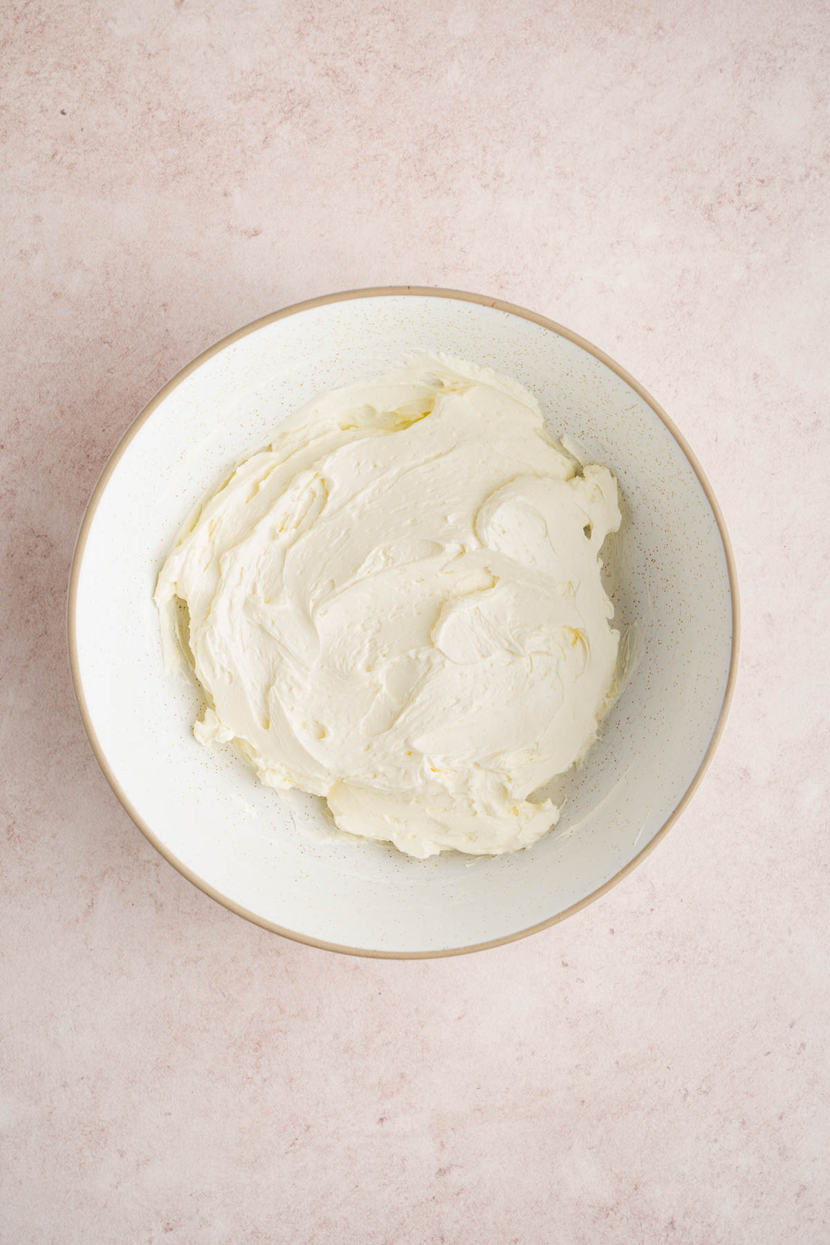 The beaten cream cheese in a white bowl on a counter.