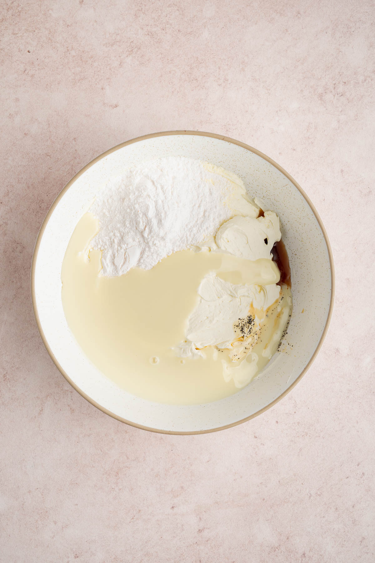 The cream cheese, condensed milk, vanilla, and dry pudding mix in a white bowl on a countertop.