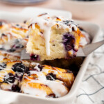 A serving utensil lifts up a piece of blueberry butter swim biscuits for serving.