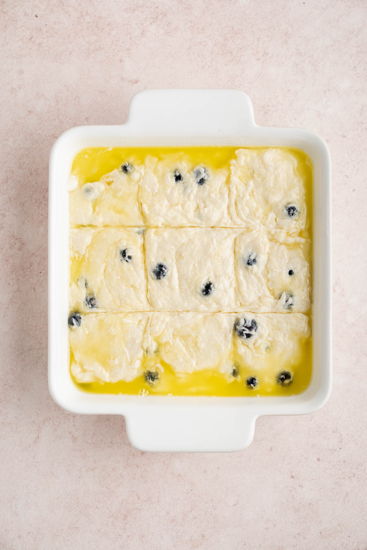 The biscuit batter in the buttered dish scored on top into 9 pieces.