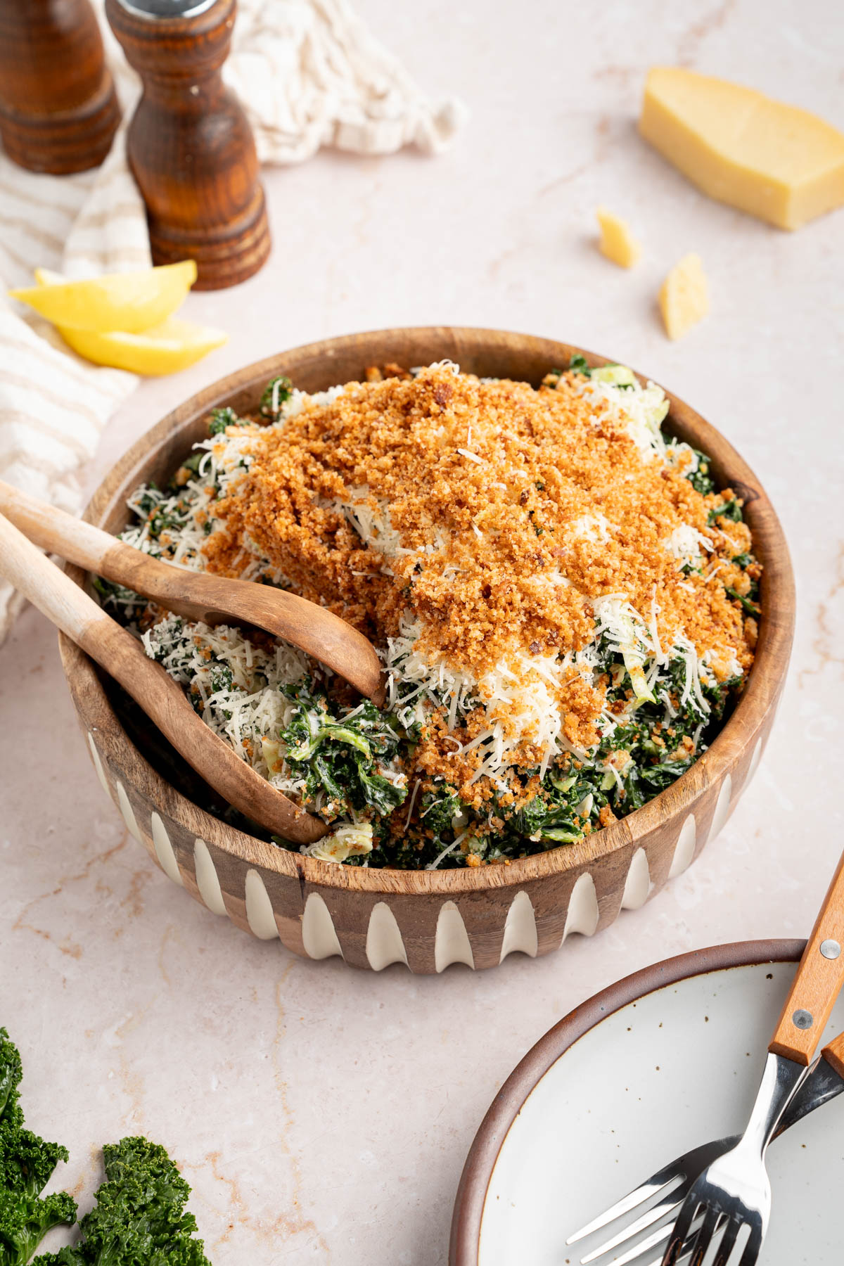 A kale caesar salad piled high in a large serving bowl with serving tongs on the side.