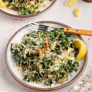 Two plates with kale caesar dressing for serving. A lemon wedge sits on the side of the plate for garnish.