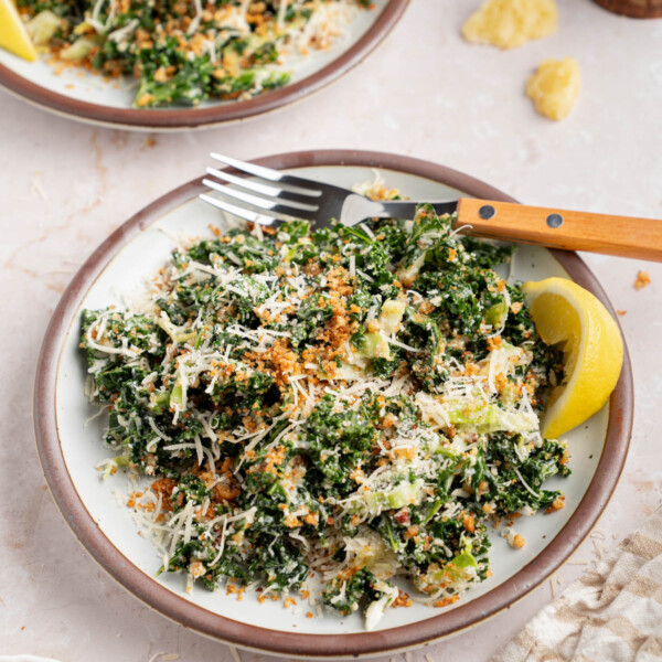 Two plates with kale caesar dressing for serving. A lemon wedge sits on the side of the plate for garnish.