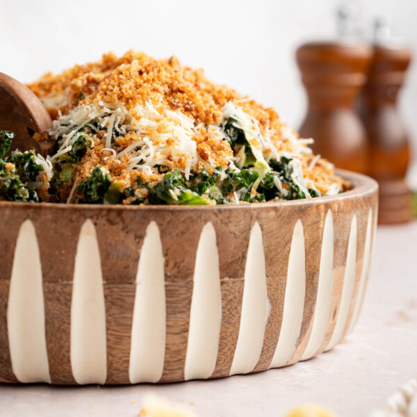 Kale caesar in a bowl with fresh shredded parmesan cheese on the kale salad and breadcrumbs on top.