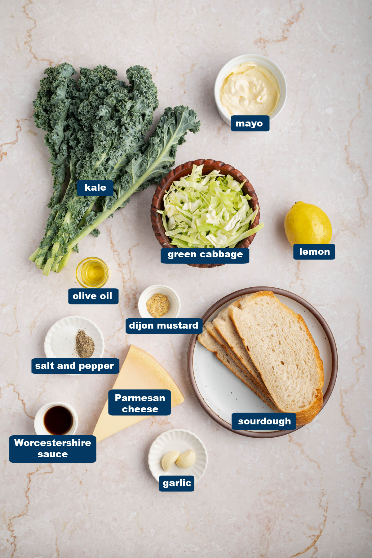 All of the ingredients for kale caesar salad in bowls on a white countertop.