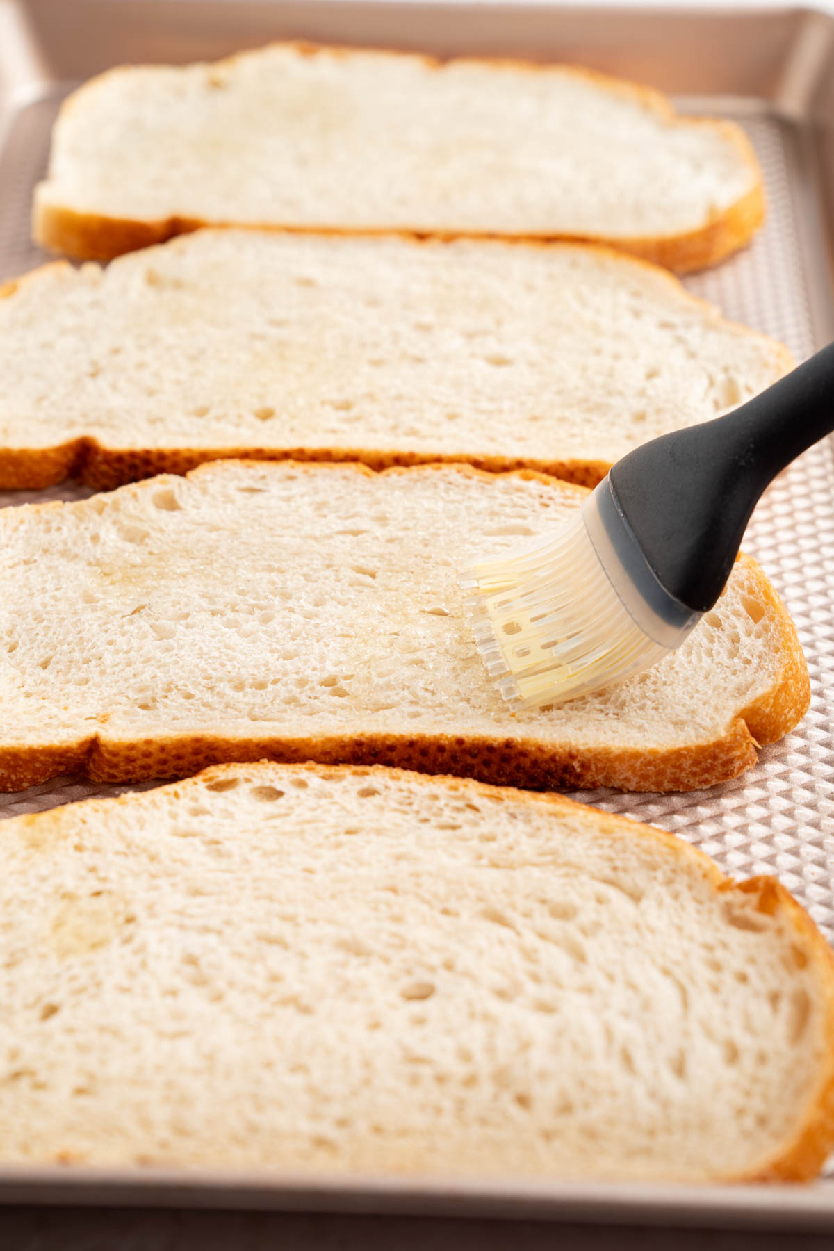 A pastry brush brushes olive oil on the bread slices before baking.