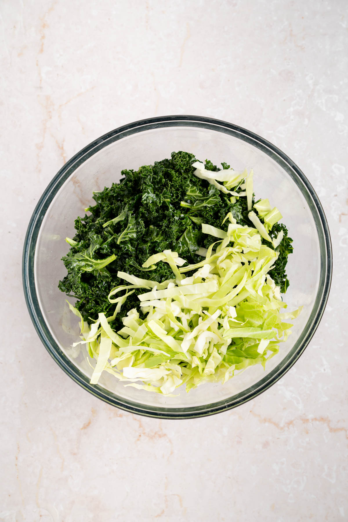 The shredded cabbage in the bowl with the massaged kale.