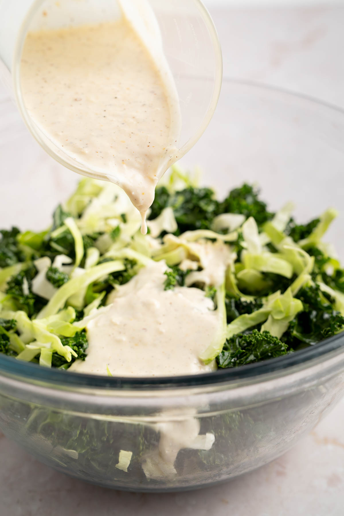 Pouring the dressing over the mixed kale and cabbage.