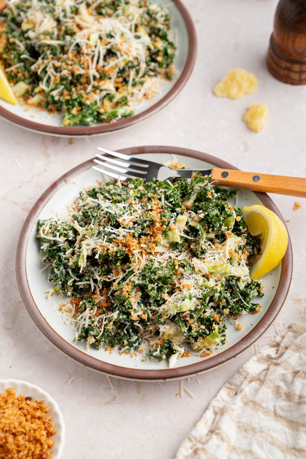 Two plates with kale caesar dressing for serving. A lemon wedge sits on the side of the plate for garnish.