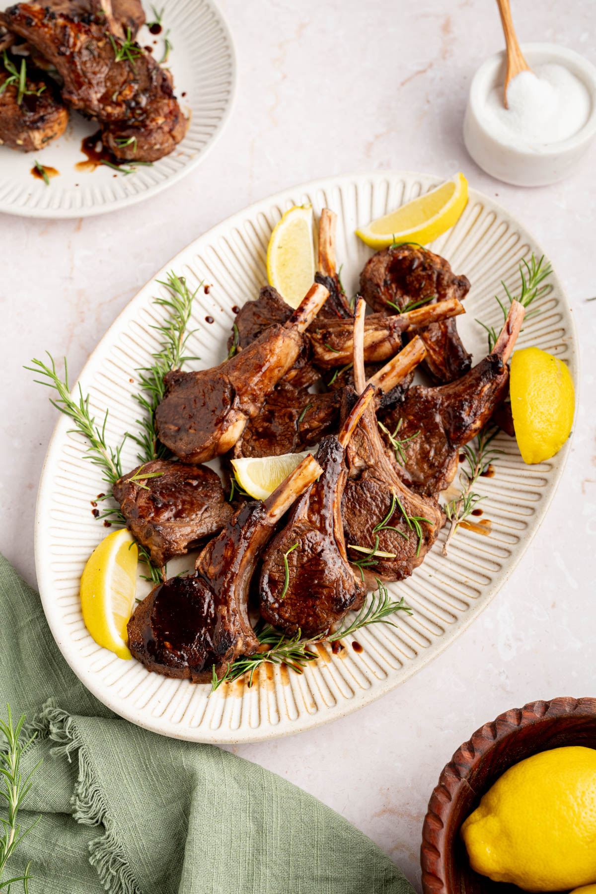 The baked lamb chops with balsamic honey glaze on a white serving plate garnished with rosemary and lemon wedges.