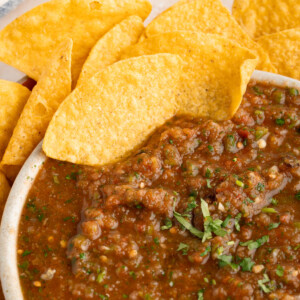 Two chips scoop chunky salsa from a bowl.