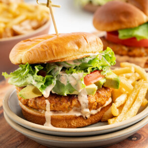 A shrimp burger on a plate with french fries.