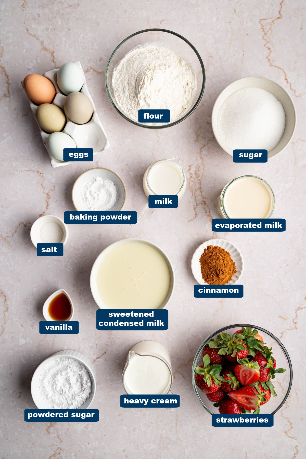All of the ingredients for tres leches in bowls on a countertop.