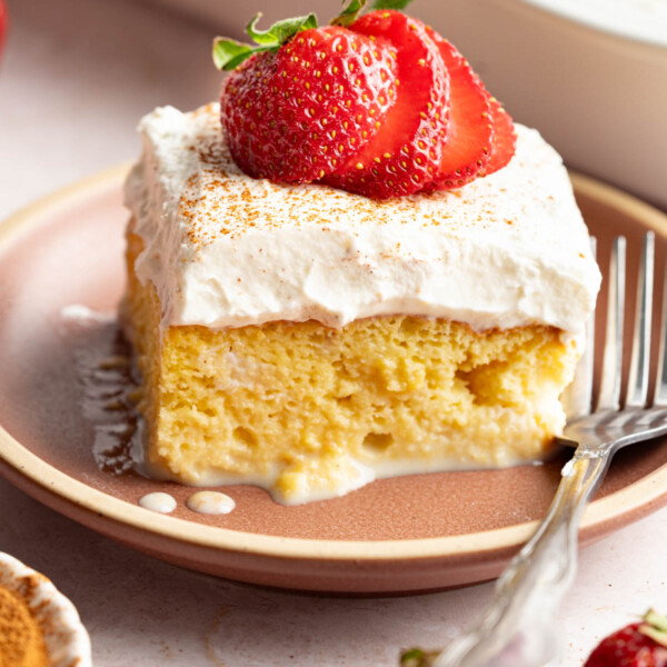 A slice of tres leches cake with a sliced strawberry on top on a plate with a fork for serving.