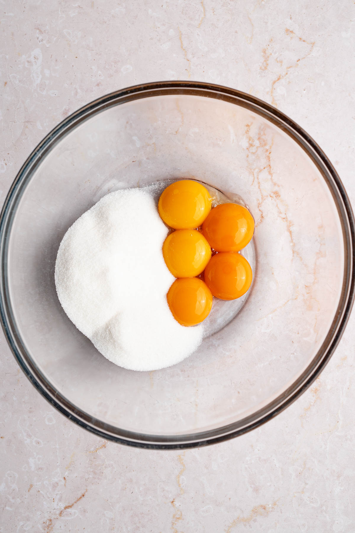 Egg yolks in a glass bowl with sugar before mixing.