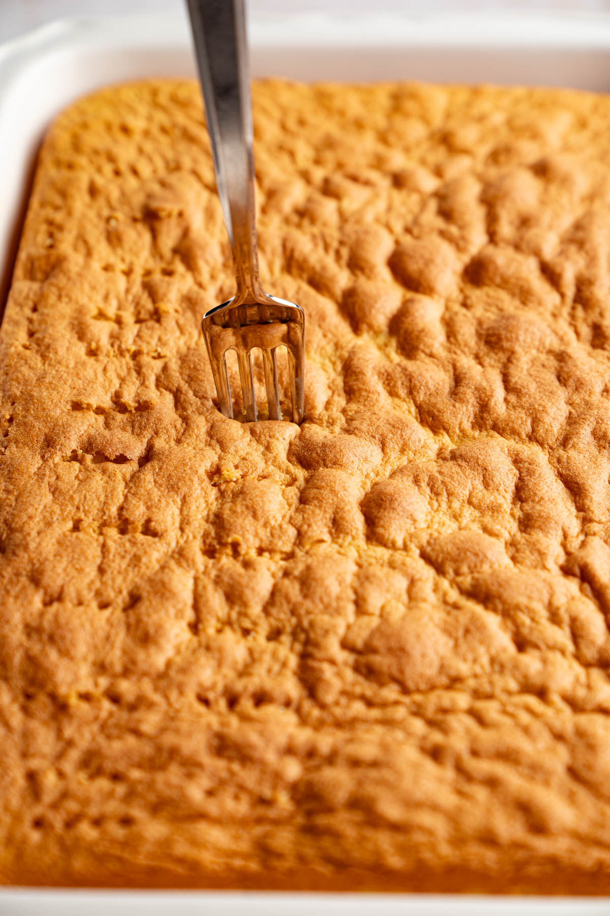 A fork poking holes in the baked cake.