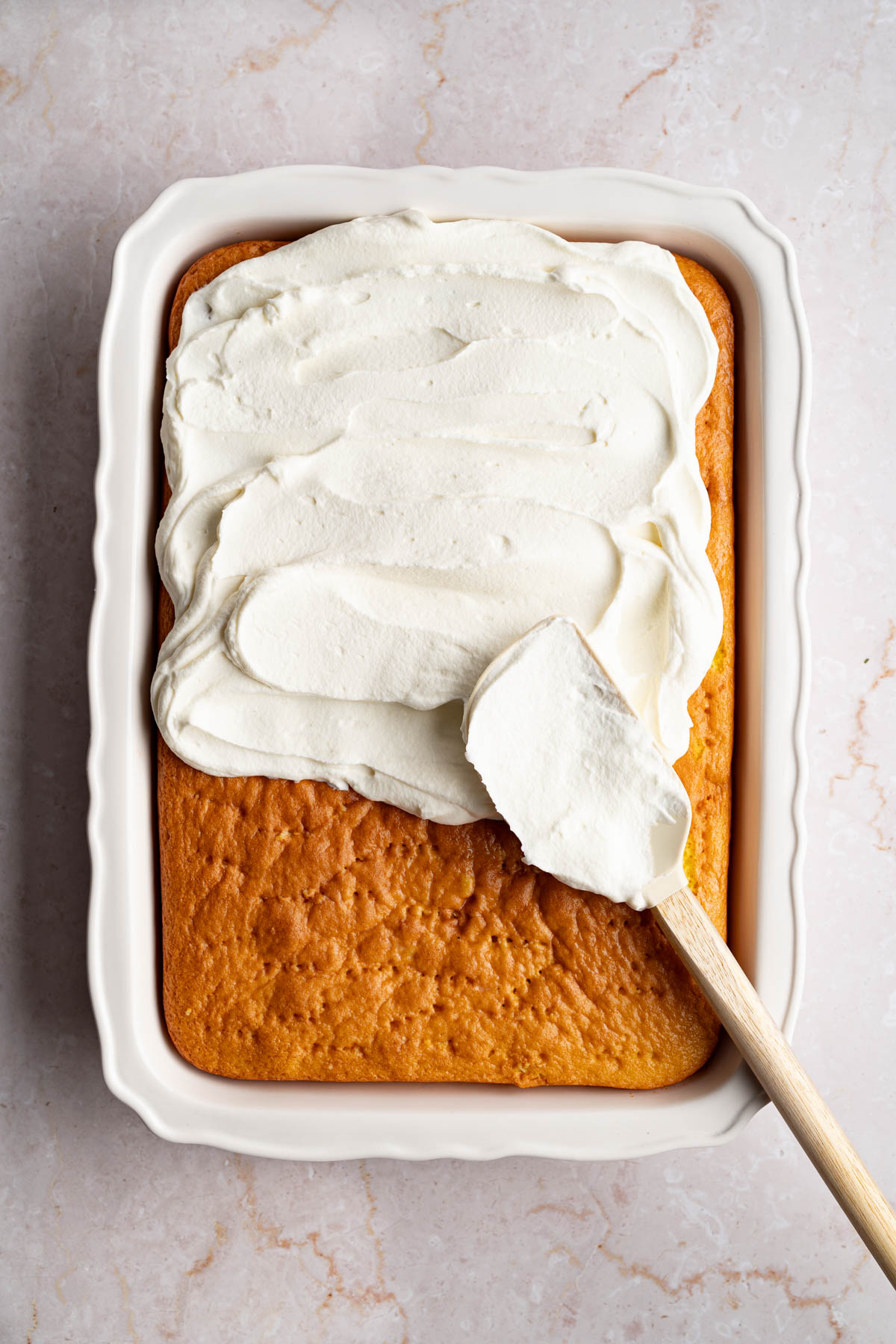 Spreading the whipped cream over the cake with a spatula.