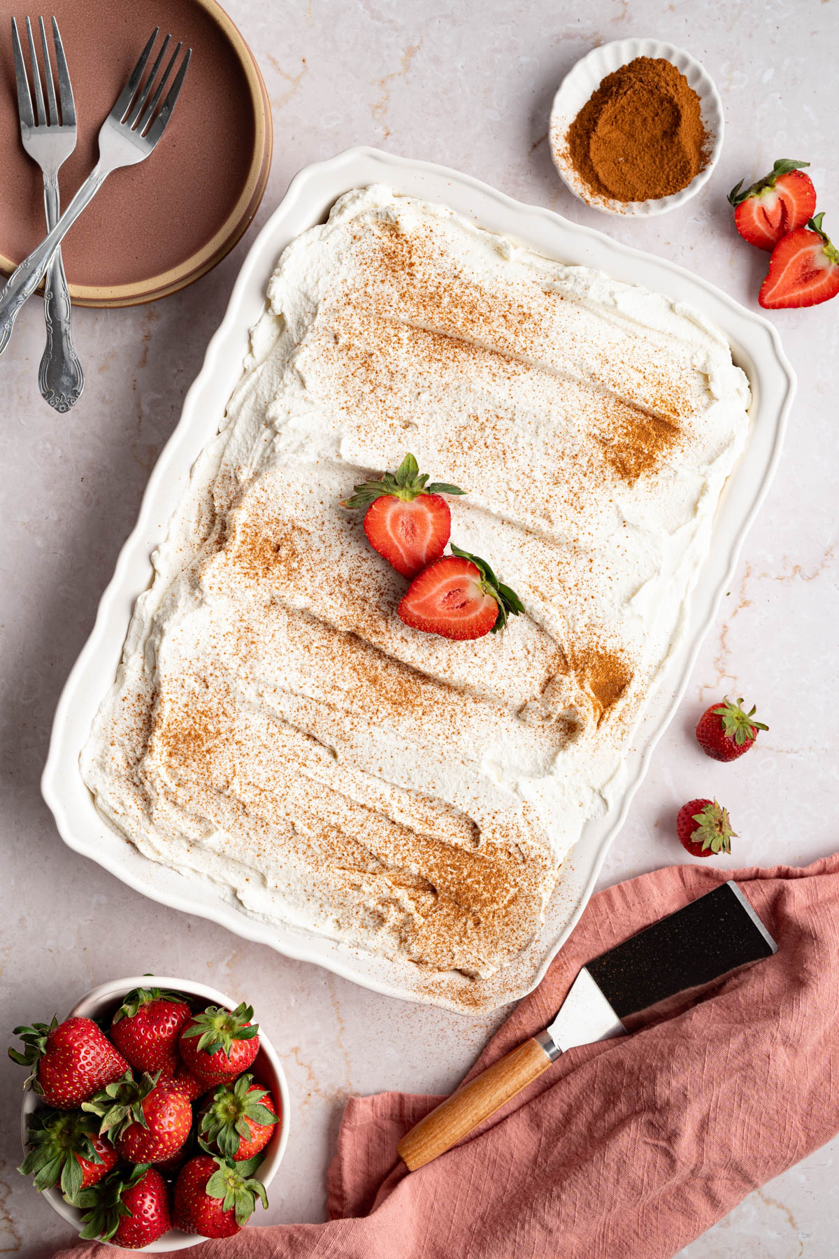Finished tres leches cake decorated with a dusting of cinnamon and cut strawberries on a white countertop.