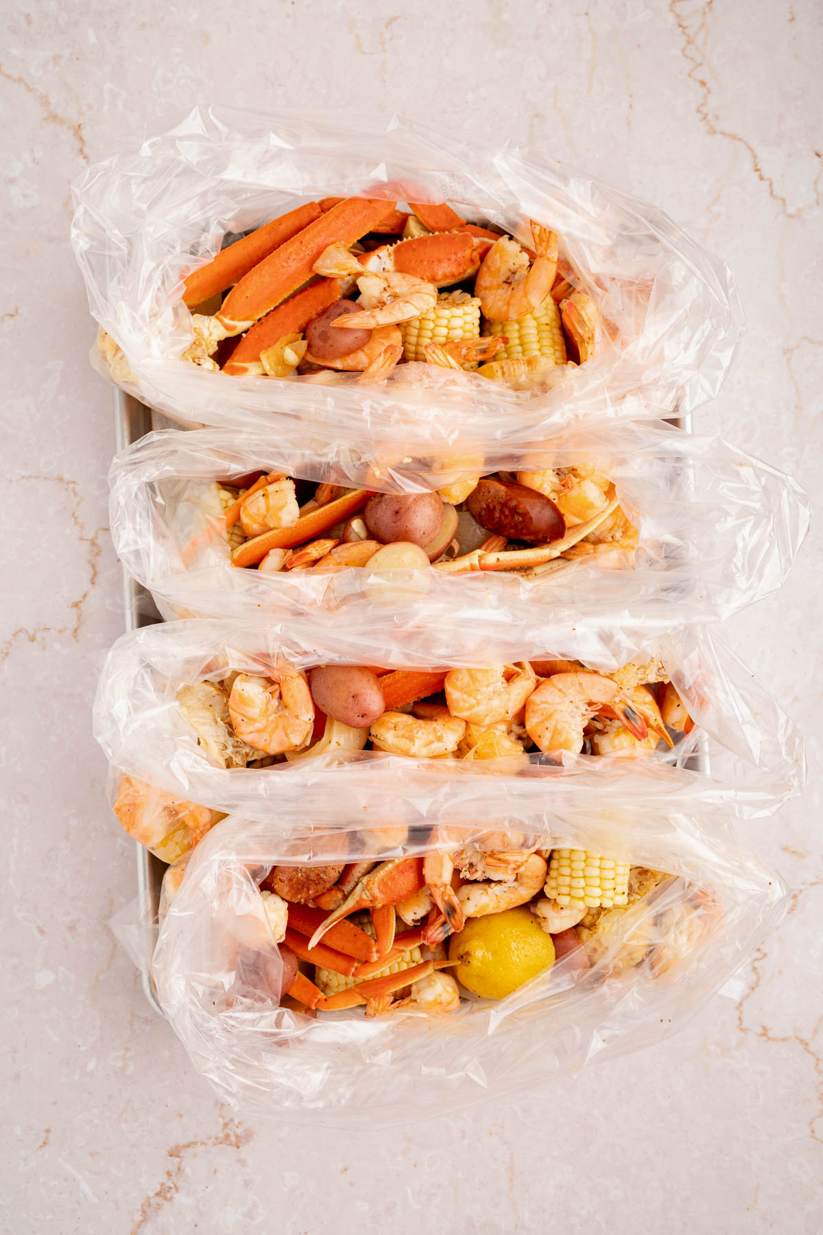 The drained seafood, corn, sausage, and potatoes divided into 4 bags on a white countertop.
