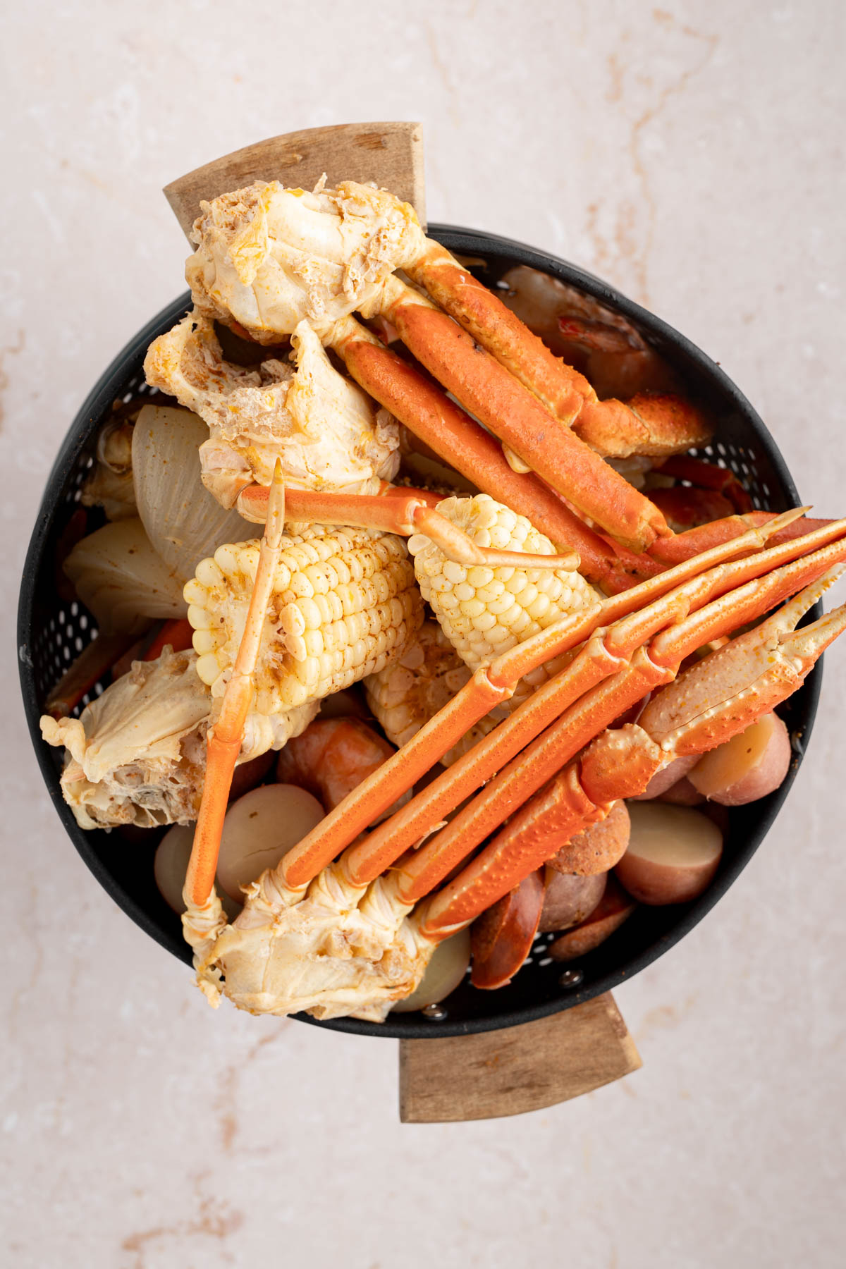 The drained corn, potatoes, shrimp, and crab claws in a colander.