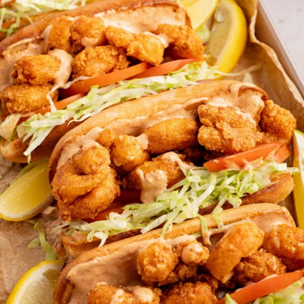 Four shrimp po boys on a baking sheet after being assembled with lemon wedges on the side.