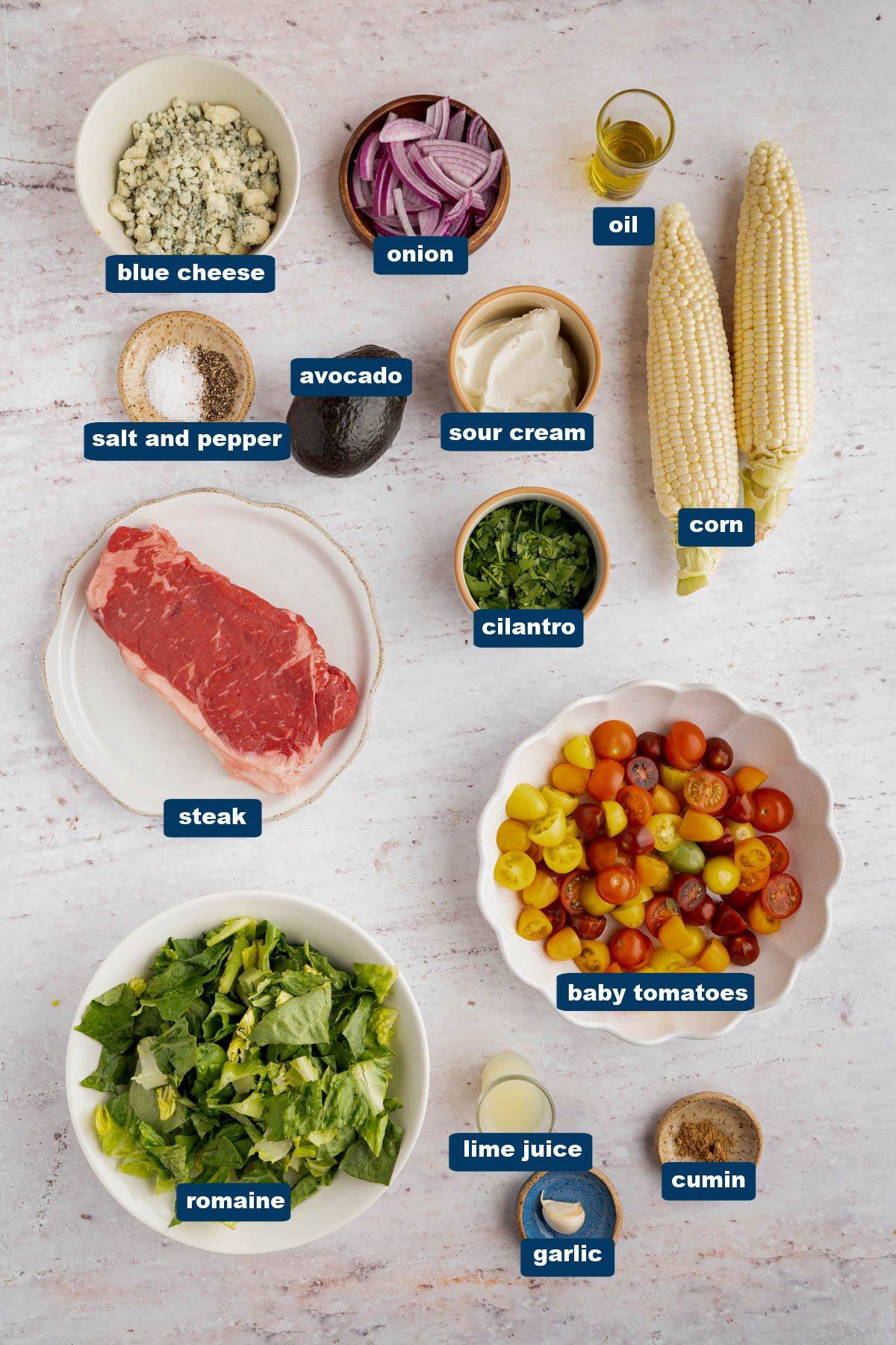 All of the ingredients for steak salad in bowls on a white countertop.